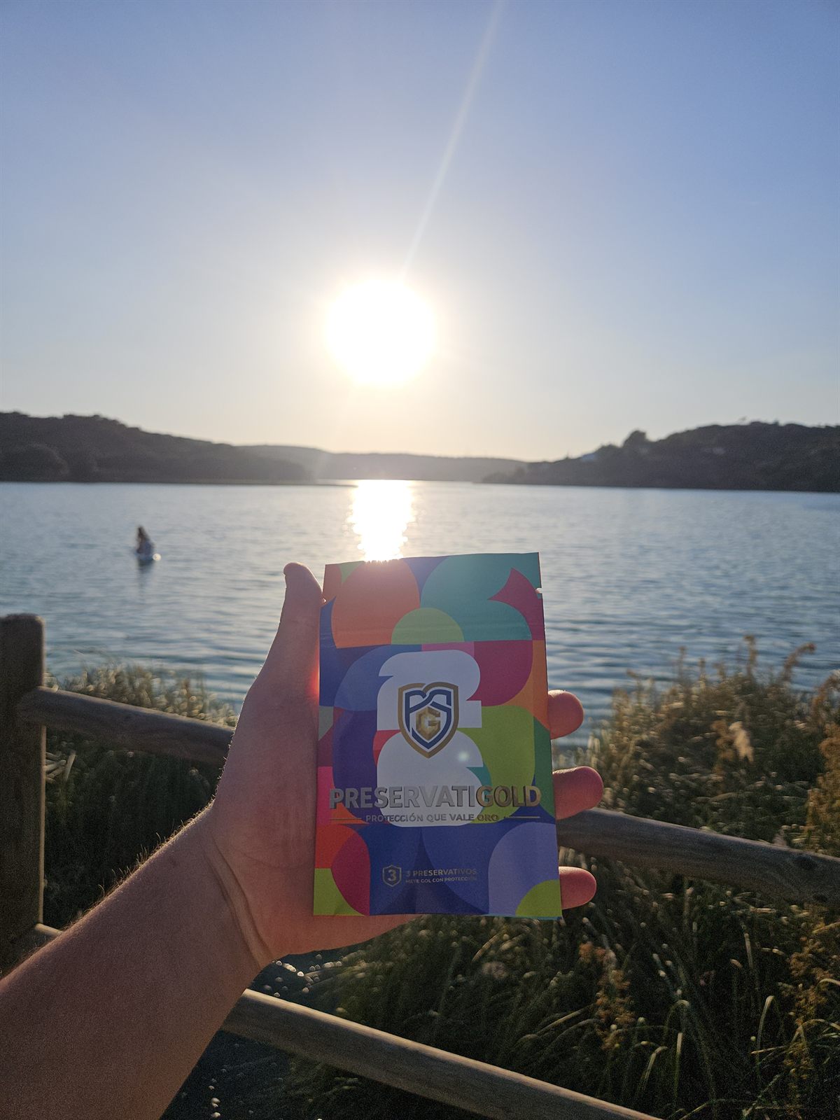 Pack PreservatiGold edición Mundial 2026 sostenido a contraluz del sol brillante sobre el mar, diseño multicolor con el escudo dorado