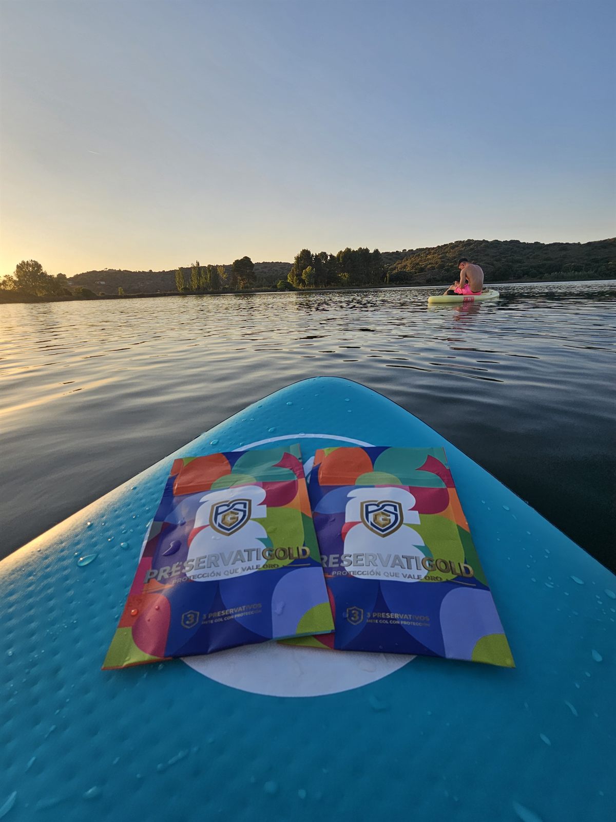 Dos packs PreservatiGold edición limitada colocados sobre una tabla de paddle con gotas de agua, al atardecer en el lago